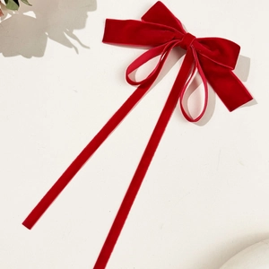 Close-up of red velvet bow hair clip with long ribbons and soft fabric texture