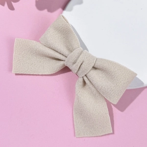 Dettaglio del fermaglio a fiocco in lana beige su un fondo rosa minimalista