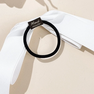 Detail of black elastic hair tie featuring a brown Hand Made fabric label and white satin