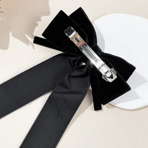 Elegant black velvet bow hair clip with long streamers on a white display stand