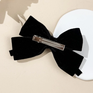 Detail of black velvet bow hair clip with silver metal alligator clip on textured background
