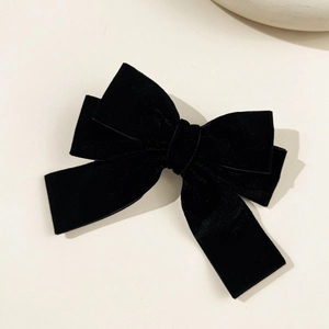 Detailed top view of a luxury black velvet double bow hair clip on a minimalist background