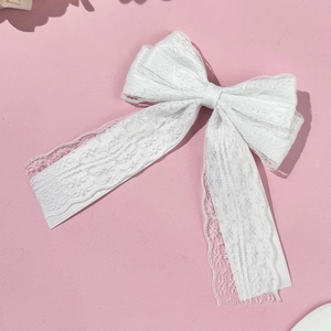 Close-up of white lace bow hair clip showing detailed floral embroidery and ribbons