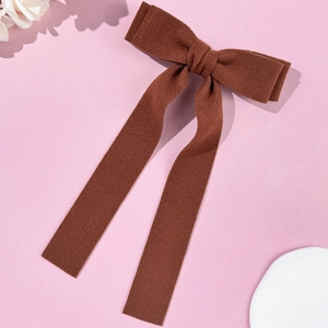Close-up of a brown velvet bow hair clip with long ribbons on a soft pink background