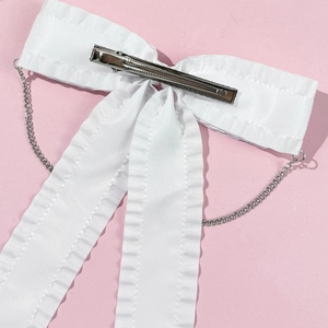 Détail du nœud en satin blanc avec chaîne argentée et pince crocodile en métal au dos