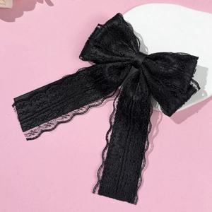 Detail of black floral lace bow hair clip with satin ribbon on white ceramic plate