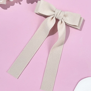 Close-up of cream white wool bow hair clip with long flowing ribbons on pink paper