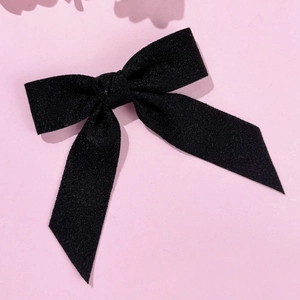 Close-up of elegant black velvet bow hair clip with detailed texture on pink background