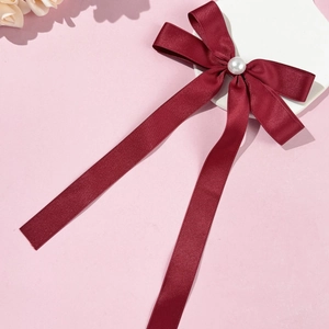 Close-up of wine red satin bow hair clip with a lustrous pearl on a white pedestal