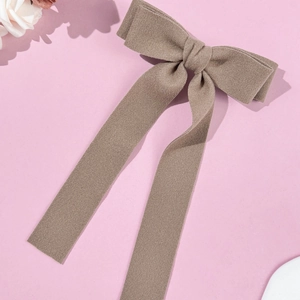 Macro shot of large taupe wool bow hair clip with elegant long ribbons on pink backdrop