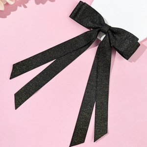 Close-up of glittery black double-layer bow hair clip with long ribbons on pink background