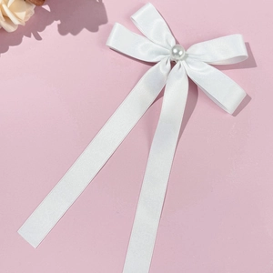 Close-up of white satin bow hair clip with center pearl and long elegant ribbons