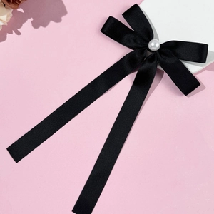 Detail of elegant black satin bow hair clip featuring a centered white faux pearl