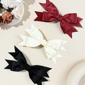 Detailed view of satin bow hair clips in wine red, cream, and black colors