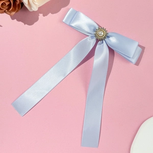 Makro-Detail einer hellblauen Satin-Haarschleife mit zentraler Perle und Strass-Einlage