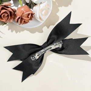 Elegant black satin bow hair clip with silver spring metal fastener on beige surface