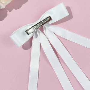Detail of white satin ribbon bow hair clip with long streamers on pink background