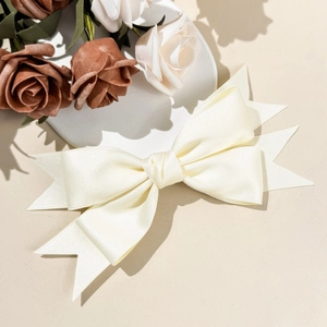 Close-up of cream satin bow hair clip with layered swallowtail design and silky texture