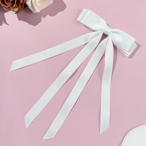 Detail of elegant white satin bow hairclip with long ribbons on soft pink background