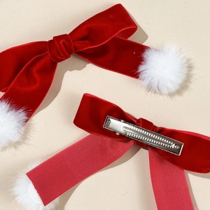 Detail view of red velvet bow hair clips with white pom-poms and silver metal duckbill clips