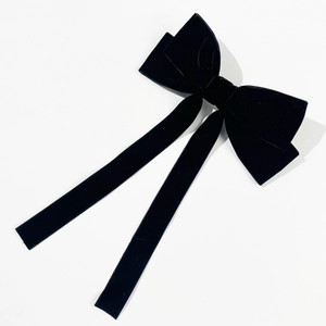 Detail of elegant black velvet hair bow clip featuring long flowing silk-like streamers