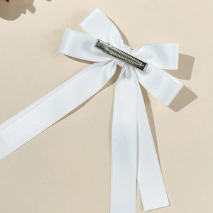 Detailed close-up of a white satin ribbon bow hair clip with an elegant long streamer design