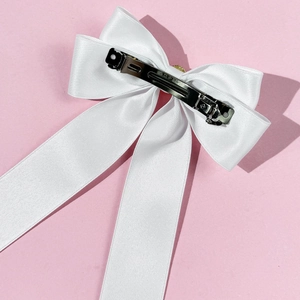 Détail du clip métallique argenté sur un accessoire de cheveux nœud en satin blanc