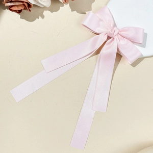 Elegant light pink satin bow hair clip with long ribbons on a decorative white plate