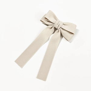 Close-up of cream bow hair clip showing textured fabric and elegant long streamers