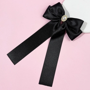 Détail d'un nœud en satin noir avec perle et strass sur fond rose pour accessoires cheveux