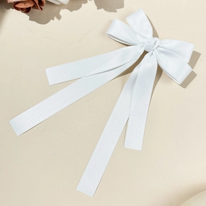 Elegant white satin bow hair clip with long ribbons on a minimalist cream background