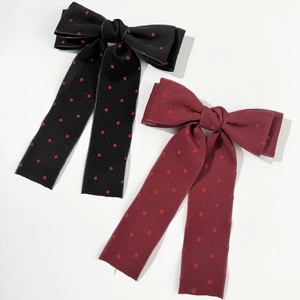 Close-up of black and burgundy bow hair clips with red polka dots on white background