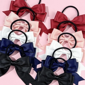 Detail showing five assorted satin bow hair ties in red, pink, white, navy, and black