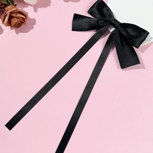 Detail of elegant black satin ribbon bow hair clip with long streamers on pink background