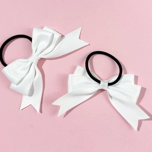 Close-up of white satin bow hair ties with black elastic bands on pink background