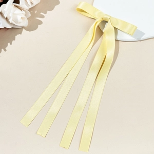 Détail d'une barrette à nœud en satin jaune pâle avec de longs rubans et texture soyeuse