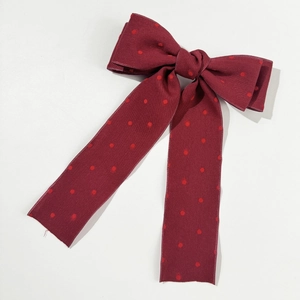 Detailed close-up of dark red polka dot bow hair clip with fine fabric texture