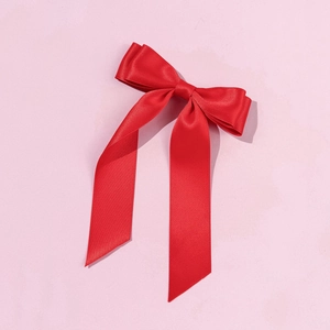 Detail view of the red satin bow hair clip with long ribbons on pink background
