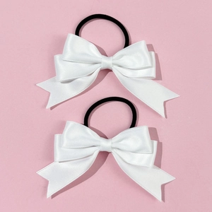 Detailed close-up of white satin bow hair tie with elastic band on pink background