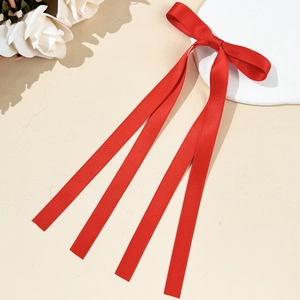 Détail d'un nœud papillon en satin rouge avec de longs rubans sur un socle blanc épuré