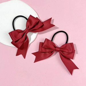 Detail of two wine red satin bow hair ties with V-cut tails on pink background
