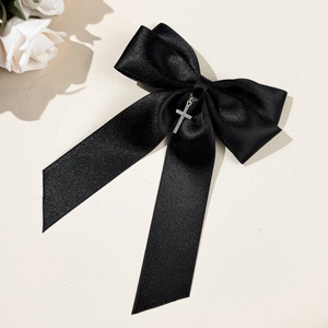 Détail de la barrette à nœud en satin noir avec pendentif croix argentée sur fond beige