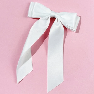 Detailed view of a white satin bow hair clip with long ribbons on pink background