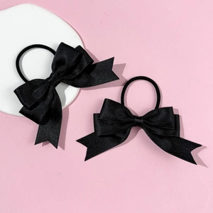 Detail of two black bow hair ties showing fine twill texture on pink background