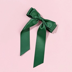 Close-up of forest green forest satin ribbon bow hair clip on a soft pink background