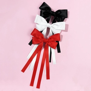 Elegant satin bow hair clips in red, white and black with long ribbon tails on pink backdrop