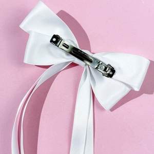 Detail view of white satin bow hair clip with silver spring mechanism on pink background