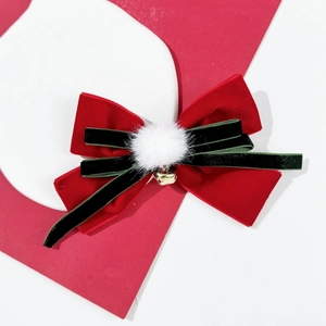 Detailed close-up of a festive red velvet bow hair clip with green ribbons and a gold bell