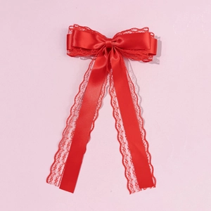 Close-up of a large red satin bow hair clip with floral lace edges and long flowing ribbons