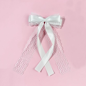 Close-up of white layered lace bow hair clip with satin ribbons on pink background